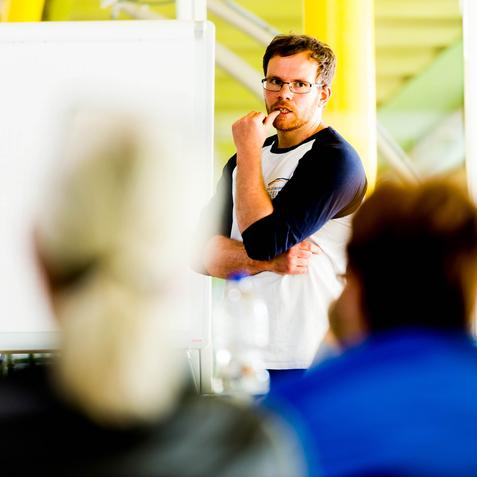 Mann mit Brille spricht vor einer Gruppe, ein Flipchart ist im Hintergrund sichtbar.